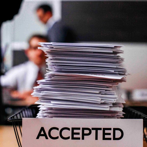 A large stack of accepted papers in a labeled tray on a desk.