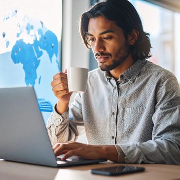 Man working on laptop while drinking coffee in a bright office.