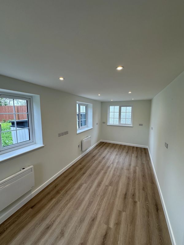 Empty narrow room with wood flooring and white walls under ceiling lights.