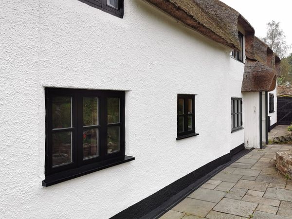 White cottage with thatched roof and black-framed windows along a stone pathway.