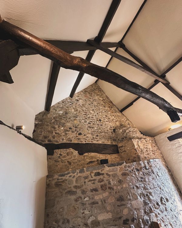 Interior view of a rustic stone wall with exposed wooden beams on the ceiling.