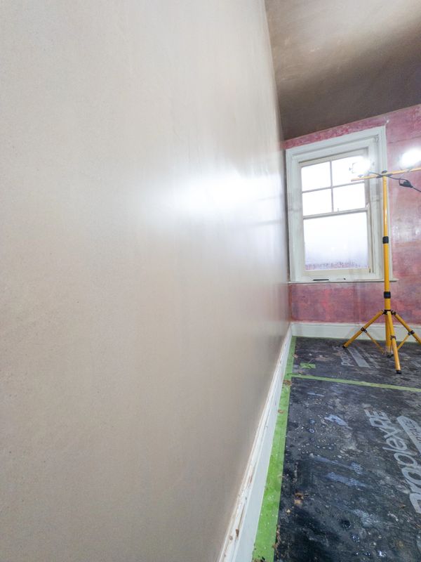A freshly plastered wall in a room under renovation with protective floor covering.