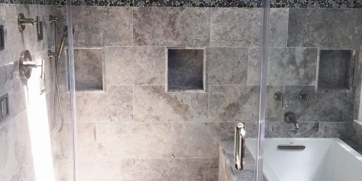 A drop-in tub in the shower enclosure with gray marble a hand shower body sprays niches circle glass