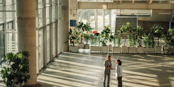 Two people talking in a spacious, sunlit modern building lobby.