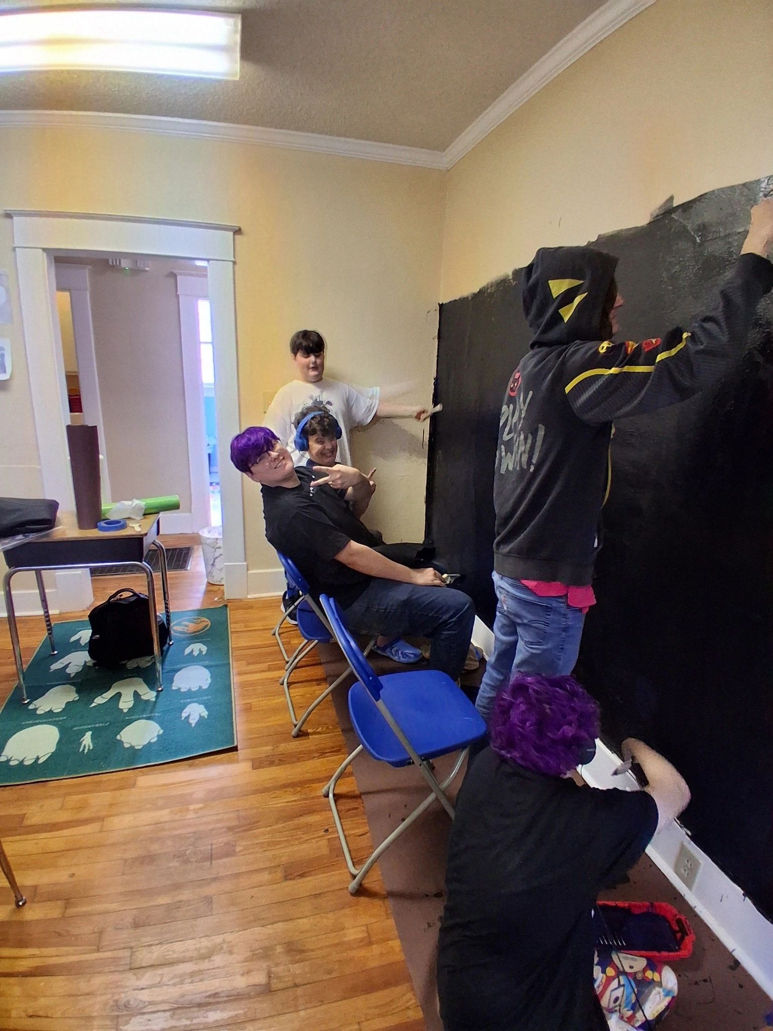 A group of young people painting a wall black in a room.