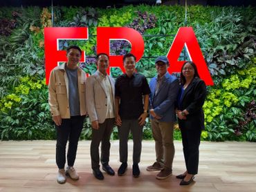 Five people posing in front of a plant wall with large red letters.