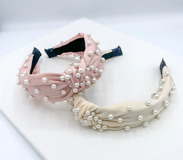 Two pearl embellished knotted headbands, one in white or cream and one in pink.