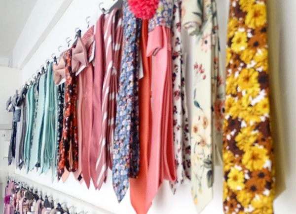 A row of hanging colourful ties and matching bow ties in black colours and floral prints.