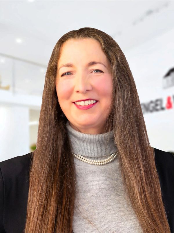Smiling woman with long brown hair in a gray turtleneck and pearl necklace.