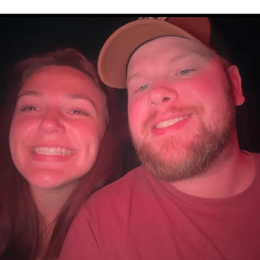 A smiling couple taking a close-up selfie in red lighting.