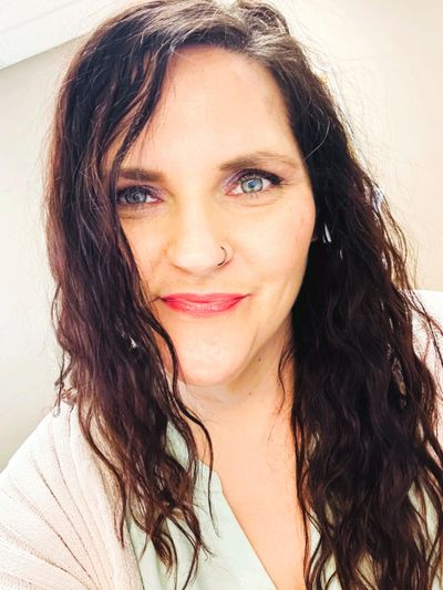 A woman with wavy brown hair and blue eyes smiling at the camera.