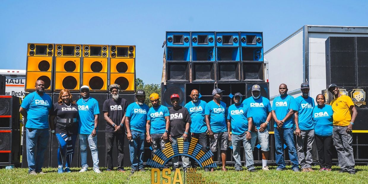 Group of people posing in front of large colorful sound system speakers outdoors.