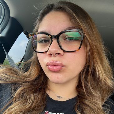 Young woman with glasses and septum piercing taking a selfie in a car.