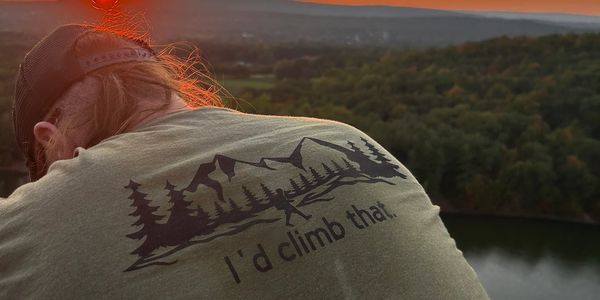 Person watching sunset wearing a shirt with mountain climbing design and text.