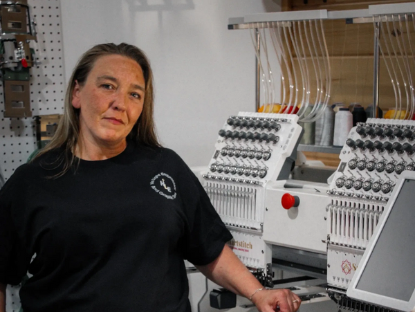 Owner Patricia Thompson standing next to the embroidery machine that makes it all happen.