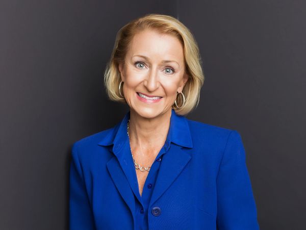 Smiling woman in a royal blue blazer against a dark background.