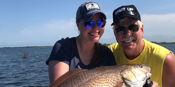 Two people holding a large fish by the water.