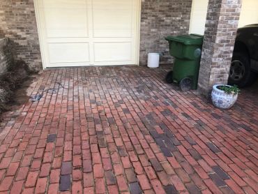 Brick driveway with green trash bin near garage.