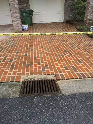 Caution tape blocking access to a brick driveway with a drain.