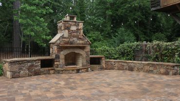 Stone outdoor fireplace with seating in a lush backyard.