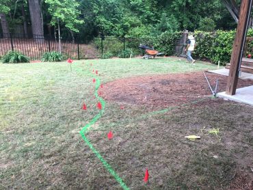 Worker in a yard with marking flags and wheelbarrow.