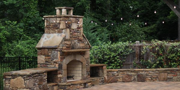 Stone outdoor fireplace with string lights and greenery.