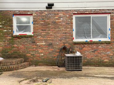 Brick wall with two windows and air conditioning unit.
