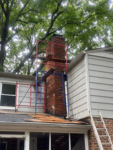 Scaffolding around a brick chimney on a house roof.