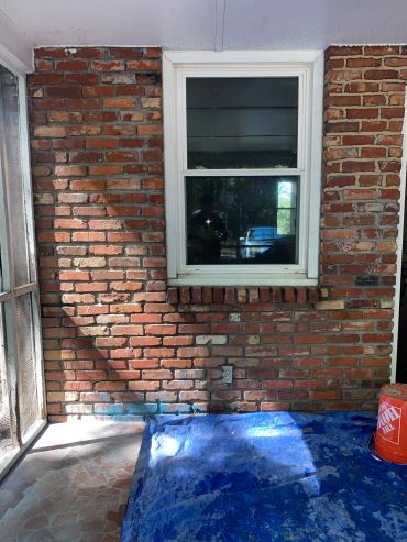 Brick wall with window and blue tarp on floor.