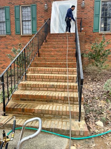 Person pressure washing brick stairs outside a house.