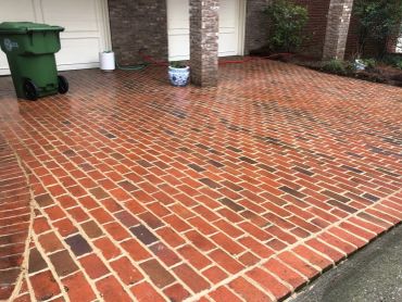 Wet red brick driveway outside a house with garage.