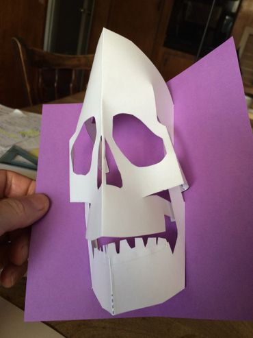 Hand holding a purple card with a white pop-up skull cutout.