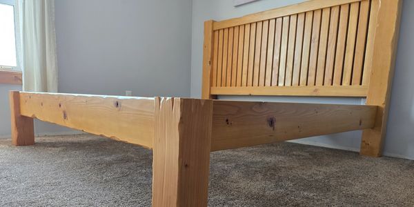 Wooden bed frame with a slatted headboard on a carpeted floor.