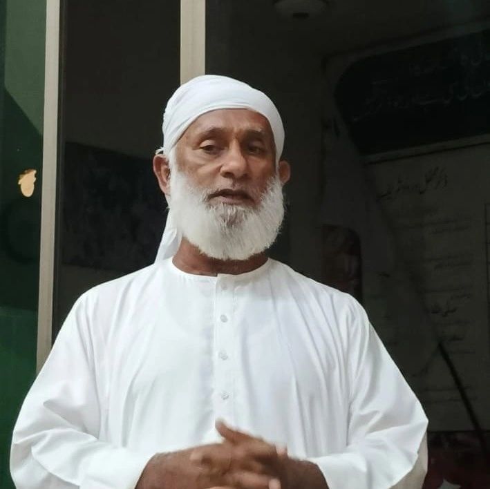 Elderly man in white traditional attire with a white beard.