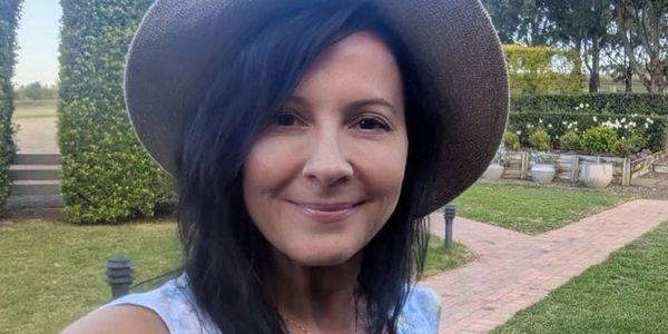 Smiling woman in a hat taking a selfie outdoors in a garden.