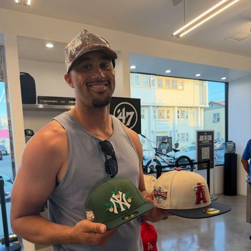 Smiling man holding two baseball caps inside a store.