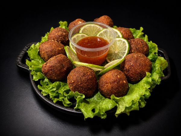 Fried balls appetizer with dipping sauce and lime slices on lettuce.