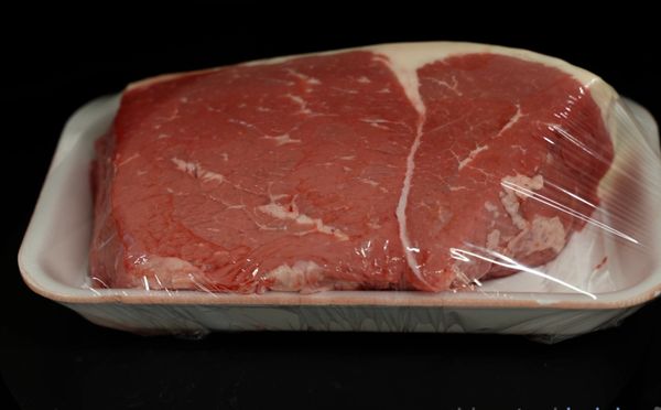 Raw beef steak wrapped in plastic on a tray.