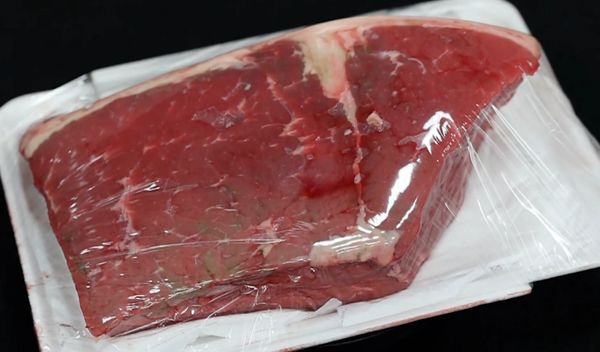 Fresh raw beef wrapped in plastic on a white tray.