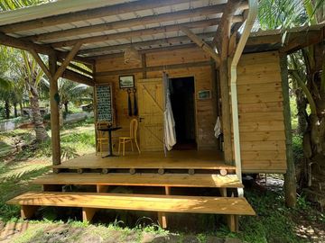 Petite cabane en bois avec terrasse et chaise sous un toit.