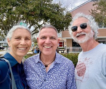 Three smiling adults posing outdoors in a friendly selfie.