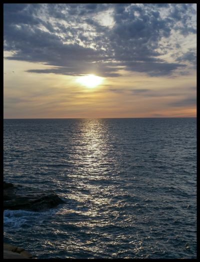 Sunset over a calm ocean with scattered clouds.