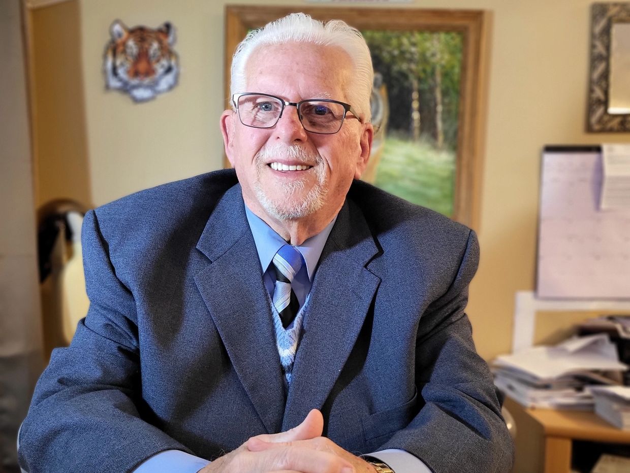 Elderly man smiling in a suit with glasses.