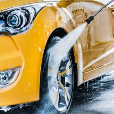 Pressure washing a yellow car's wheel.