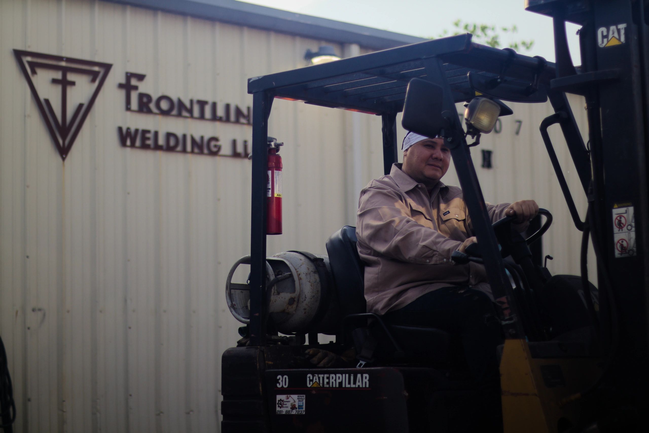 Frontline Welding worker operating a forklift in front of the company logo at our Houston facility
