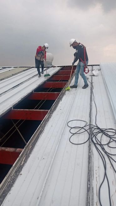 Dos trabajadores con casco limpiando un techo metálico.