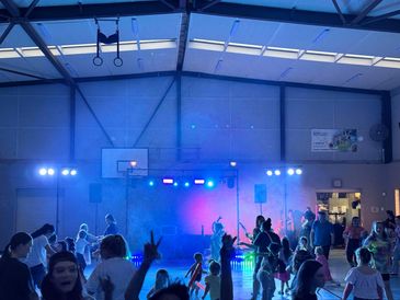 Children dancing and playing in a gym with colorful lights and music.