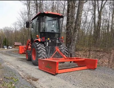 Orange tractor on a gravel road in a wooded area.