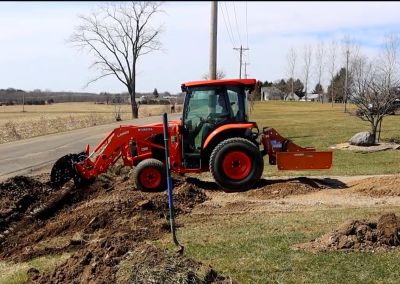 Orange tractor digging soil in a field.