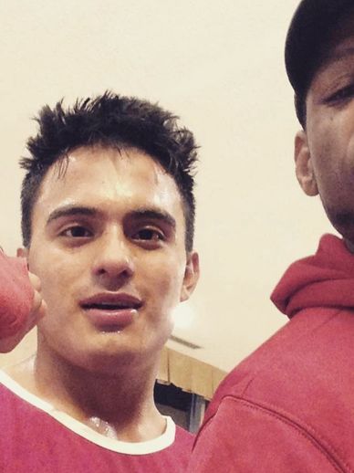 Two young men, one wearing a red sports outfit, appear indoors.